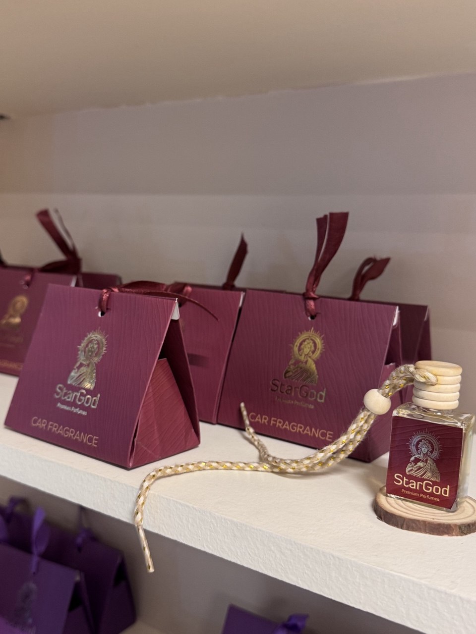 Burgundy triangular gift boxes for car fragrances on a boutique shelf, with one 10ml bottle propped on a wooden disc.