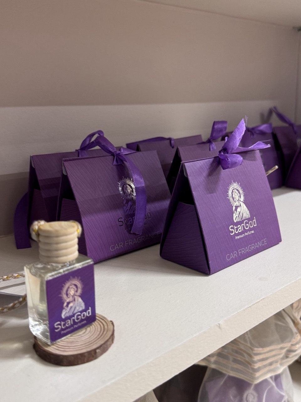 Purple triangular gift boxes lined up on a shelf with one 10ml glass bottle on a wooden disc.