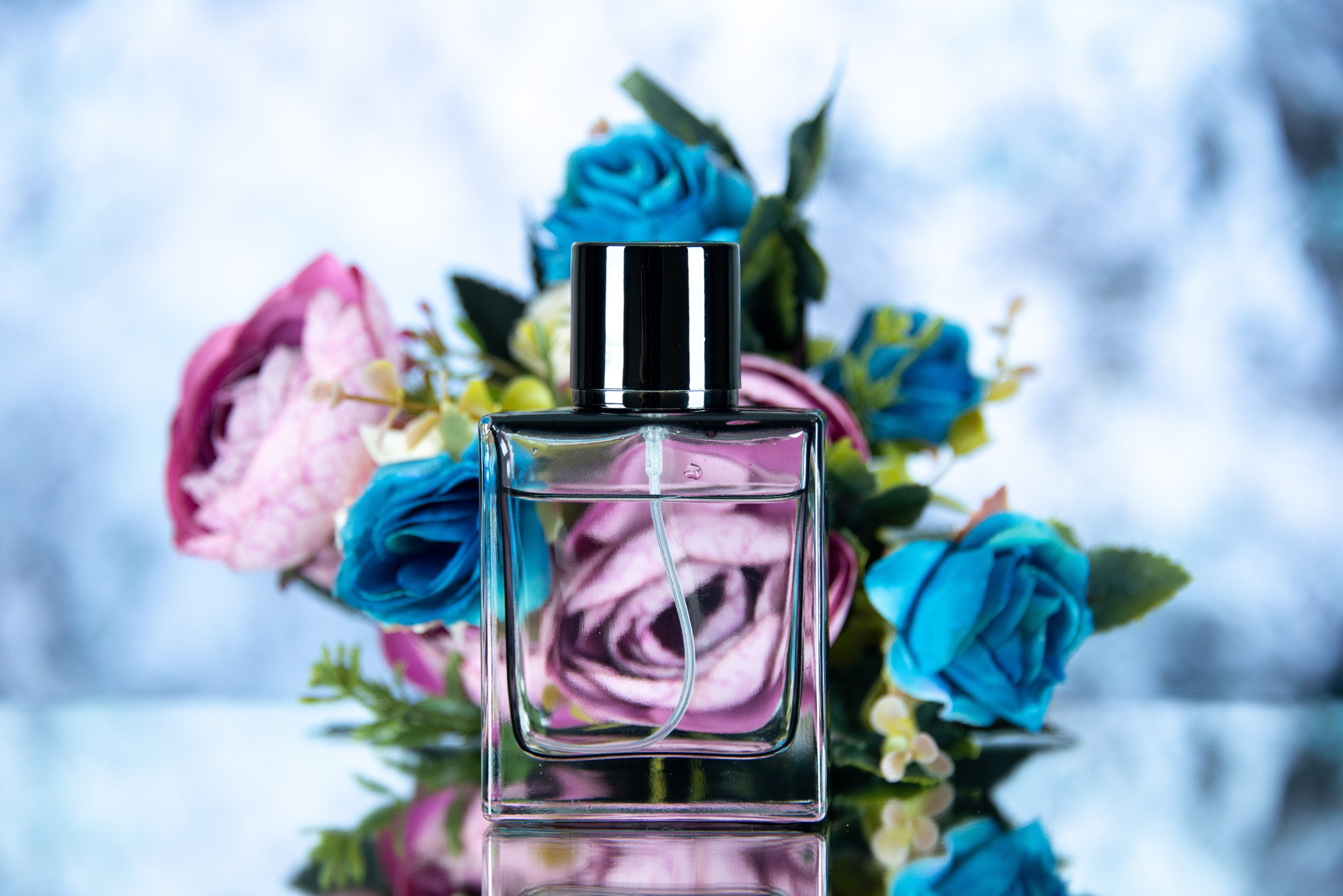 A clear-glass perfume bottle backed by a soft cluster of florals, lit warm — the kind of stillness a fragrance counter holds.